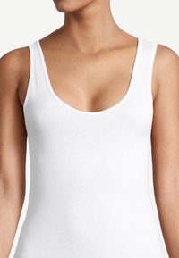 Femme portant un débardeur blanc simple sans manches avec un col rond, mettant en valeur le haut de la poitrine et les épaules.