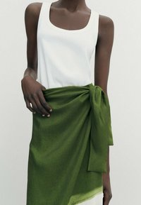 Witte mouwloze tanktop gecombineerd met een groene textuurwrap, geknoopt in de taille, met een gladde afwerking en zachte stof.