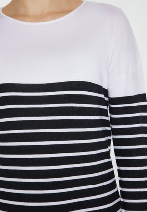 Tricou cu dungi alb-negru, cu mâneci lungi și decolteu rotund, având partea superioară complet albă și dungi orizontale alternând alb-negru în partea de jos.