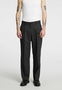 Dopasowane czarne spodnie o wysokim stanie, z podwójnymi fa�łdami z przodu, zapięciem na guziki oraz bocznymi kieszeniami, wykonane z gładkiej tkaniny.
