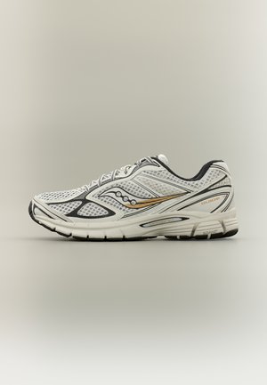 Črno-bela tekaška čevlja z zlatim logotipom, mrežastim zgornjim delom, oblazinjeno podplatom in napisom "Guide" na strani, prikazana v profilu na nevtralnem ozadju.