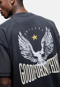 Zwarte oversized t-shirt met een witte arendgrafiek en gouden ster, met de tekst "GOODFORNOTHING" onderaan in versleten letters.