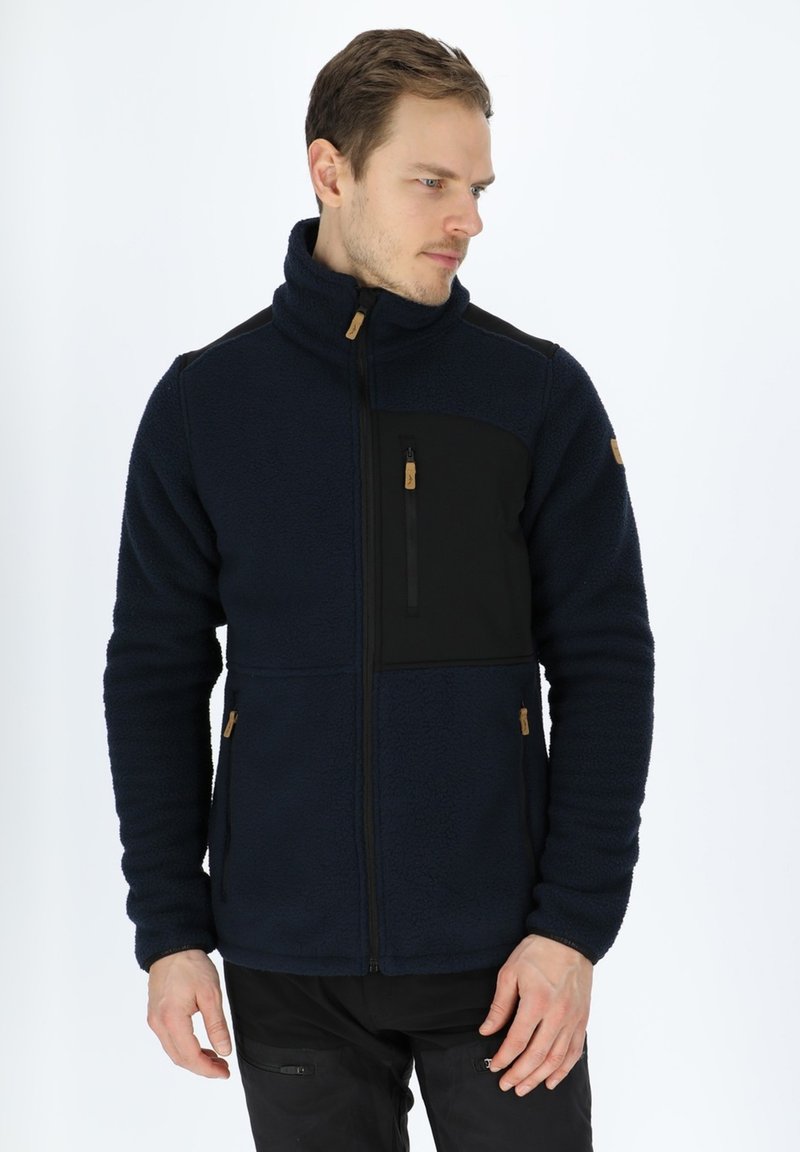 Giacca in pile di colore blu navy scuro con un pannello nero, colletto alto, tasca sul petto con zip e dettagli color sabbia. Presenta un tessuto testurizzato e un design aderente.
