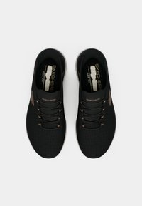 Μαύρα παπούτσια Skechers slip-on με υφή, διακοσμημένα με καφέ λεπτομέρειες, στρογγυλή μύτη και επένδυση με μαξιλαράκι για άνεση.