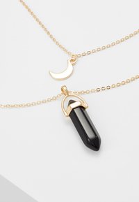 Guldtonet halskæde med en halvmånecharms og en sort krystalpendant med spids. Dobbelt kædedesign, glat og elegant.