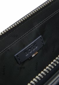 Svart tygplånboksinteriör med en framträdande präglad 'BOSS'-logotyp, dragkedjestängning och flera fack för organisering.