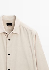 Beige kordflorskjorta med klassisk krage, dekorerad med svarta knappar och en subtil vertikal ribbstruktur. Märke: Massimo Dutti.