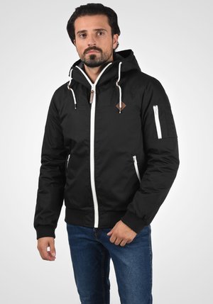 Black hooded jacket with white zipper, drawstrings, and brown leather accents. Features side and arm pockets, fitted cuffs.