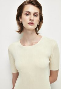 Suéter de manga corta de color crema, con un cuello redondo y tejido texturizado, que presenta un diseño ajustado y un ligero estiramiento.