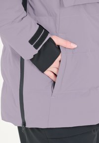 Lys lavendel isoleret jakke med sorte detaljer. Har en lynlåslomme og velcro-lukning på mansjetten. Glat tekstur.