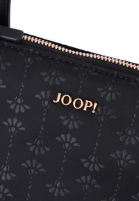 Borsa in tessuto nero con motivo floreale, logo "JOOP!" in tonalità dorata e zip dorata. Presenta una consistenza liscia e un design compatto.