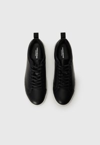 Scarpe atletiche nere in pelle con texture liscia, allacciatura frontale e suole in gomma bianca. Nessun motivo distintivo o hardware aggiuntivo visibile.