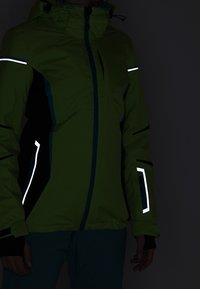 Zelená voděodolná bunda s reflexními akcenty, černými a tyrkysovými detaily, kapsami na zip a kapucí. Texturovaná tkanina, ležérní design.