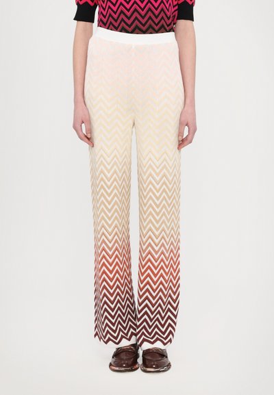 Pantalones de pierna ancha con un patrón texturizado en zigzag, que presenta un degradado de crema a marrón rojizo. Cintura elástica, combinados con zapatos oscuros.