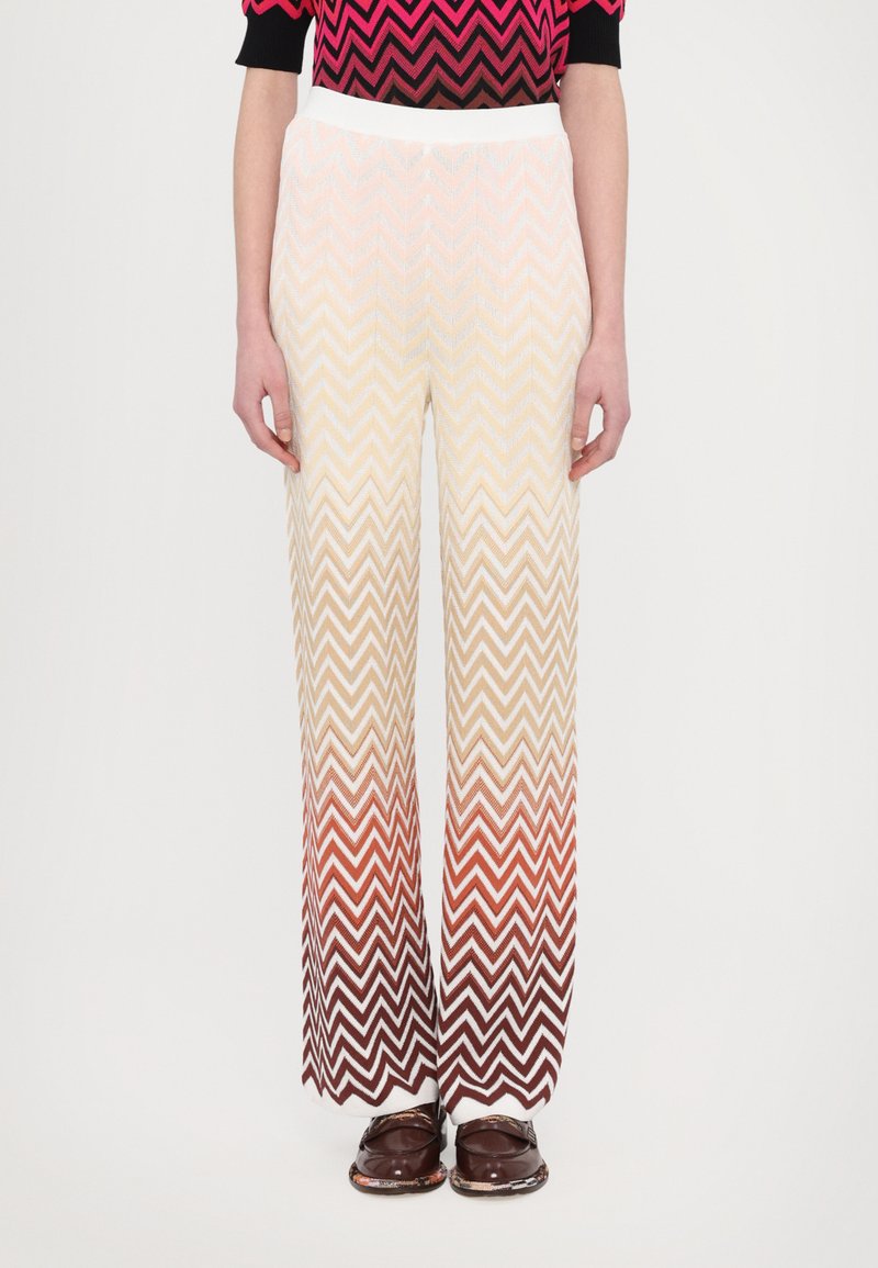Pantalons à jambes larges avec un motif en zigzag texturé, présentant un dégradé de crème à brun rougeâtre. Ceinture élastique, associés à des chaussures foncées.