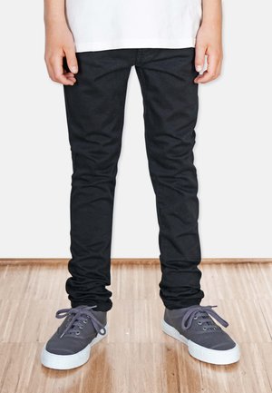 Mustat denim-farkut slim fit -mallilla, joissa on sileä rakenne. Yhdistetty harmaisiin nauhakenkiin ja valkoiseen T-paitaan.