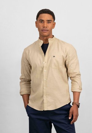 Beige overhemd met lange mouwen en een bandkraag, met knopen aan de voorkant en een borstzak met een klein donker logo. De stof lijkt textuur te hebben.