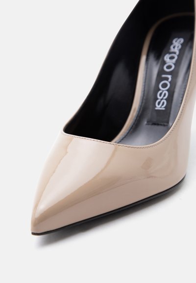 Μπεζ μυτερή γόβα με ψηλό τακούνι από δερμάτινο λουστρίνι, με μαύρο εσωτερικό και ετικέτα «sergio rossi» στο εσωτερικό.