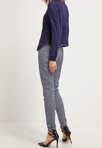 Suéter de punto color navy con diseño texturizado, combinado con pantalones ajustados azules y blancos de estampado; modelo llevando tacones altos negros con tiras.