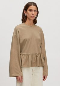 Langärmliges, taupefarbenes Baumwolloberteil mit einem Peplum-Silhouette, Rundhalsausschnitt und voluminösen Ärmeln. Glatte Textur mit einem subtilen Fall.