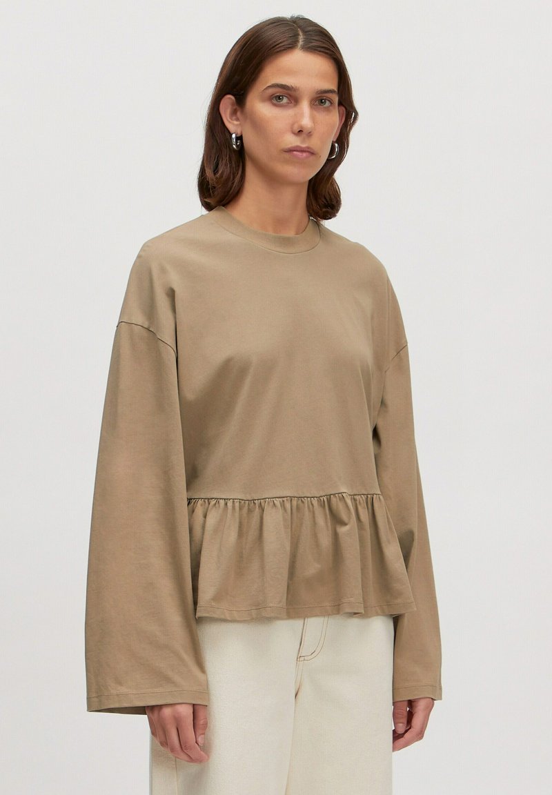 Langärmliges, taupefarbenes Baumwolloberteil mit einem Peplum-Silhouette, Rundhalsausschnitt und voluminösen Ärmeln. Glatte Textur mit einem subtilen Fall.