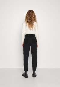 Pantaloni neri trapuntati con una vestibilità slim, dotati di tasche posteriori e un motivo testurizzato. Abbinati a stivali neri alla caviglia.