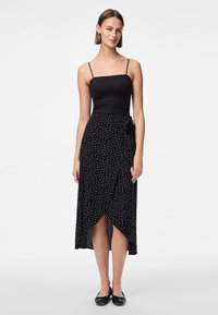 Melnā bezpiedurkņu blūze saskaņota ar melnu ietvertu svārku, kas rotāta ar baltajiem punktiņiem, no gludas auduma un ar asimetrisku apakšmalu. Melnas plakanās kurpes.