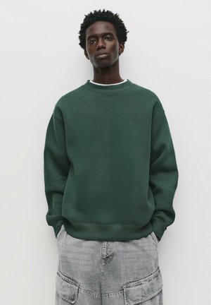 Grøn crewneck sweatshirt med en struktureret overflade, parret med lysegrå cargo shorts med flere lommer og en afslappet pasform.