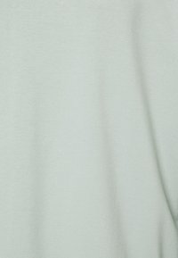 Tela de algodón verde claro con una textura suave, que cae delicadamente. Sin patrones ni elementos visibles, presentando un diseño simple y minimalista.