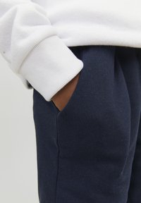 Navy puuvillaiset joggerit, joissa on sivutaskut ja pehmeä rakenne, yhdistetty valkoiseen fleece-sweatshirtin, jossa on ribbauskankaiset hihat.