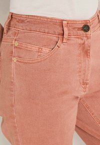 Jean en denim rose avec un design classique à cinq poches, accastillage doré et coupe slim avec une finition texturée.
