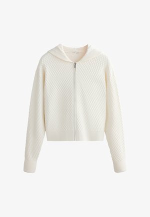 Bela pletena jopa z zadrgo, teksturiranim vzorcem diamantov, dolgimi rokavi in rebrastimi manšetami ter spodnjim robom.