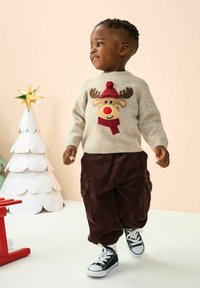 Beige Wolle Pullover mit Rentierdesign, das eine rote Mütze und Nase zeigt. Dazu passende dunkelbraune Cordhosen und schwarze Sneaker runden das Outfit ab.