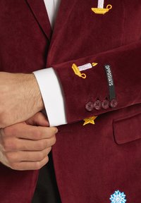 Burgundy corduroy blazer with embroidered yellow candles, a star, and a snowflake; features a white shirt cuff and four maroon buttons.