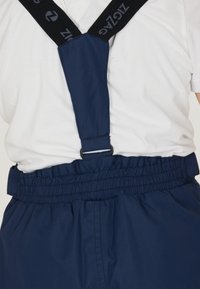 Navyblauwe overalls met verstelbare zwarte banden met een logo. Elastische taille met geplooid stofdetail voor pasvorm en comfort.