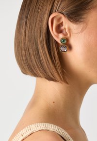 Boucles d'oreilles dorées mettant en valeur deux pierres carrées empilées : une pierre verte profonde en haut et une pierre violette en bas, toutes deux avec des surfaces facettées.