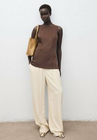 Hnedý bezrukávový top skombinovaný s krémovými nohavicami s širokými nohavicami a pieskovou kabelkou; vzorované topánky dotvárajú outfit. Minimalistický dizajn.