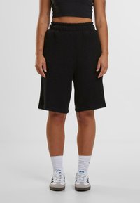 Svarta ribbade shorts med elastisk midja, knälånga, i kombination med vita strumpor och sneakers. Slät textur, avslappnad design.