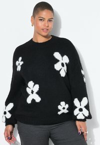 Zwart gebreide trui met witte bloemenpatronen, ronde halslijn en brede mouwen. De trui heeft een gestructureerde afwerking en een ontspannen pasvorm.