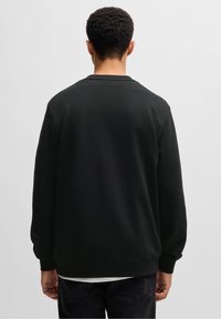 Sudadera negra hecha de tela suave, con mangas largas, cuello redondo y un corte holgado, con puños y dobladillo acanalados.