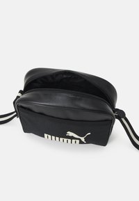 Schwarze Schultertasche mit Reißverschluss, glattem Kunstleder-Obermaterial, Stoffboden und weißem Puma-Logo sowie gestreiftem Schultergurt.