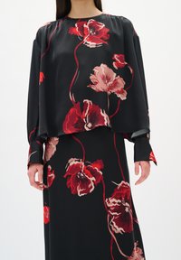 Blusa nera a maniche lunghe e gonna con grandi motivi floreali rossi e rosa, indossata da una persona mostrata dalle spalle a metà coscia.