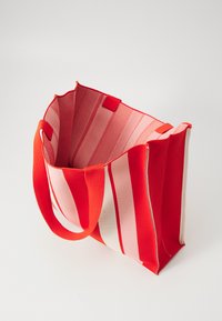 Red and pink striped tote bag with a sturdy fabric construction, open top, and two short handles for easy carrying. Interior shows mesh texture.