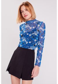 Haut bleu transparent à manches longues avec des motifs floraux, associé à une mini jupe noire dotée d'une fermeture éclair sur le côté et d'un design évasé.