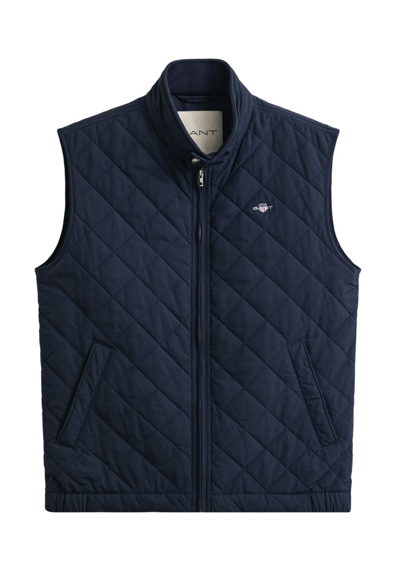 Chaleco acolchado azul marino con cuello alto, cremallera frontal y dos bolsillos laterales. Presenta un patrón de diamantes y un pequeño logotipo en la parte superior izquierda.