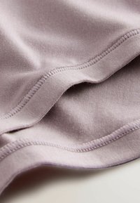 Svijetlopurple tkanina s glatkom teksturom i vidljivim detaljima šivanja, presavijena kako bi pokazala obline i rubove, naglašavajući mekoću i fleksibilnost.