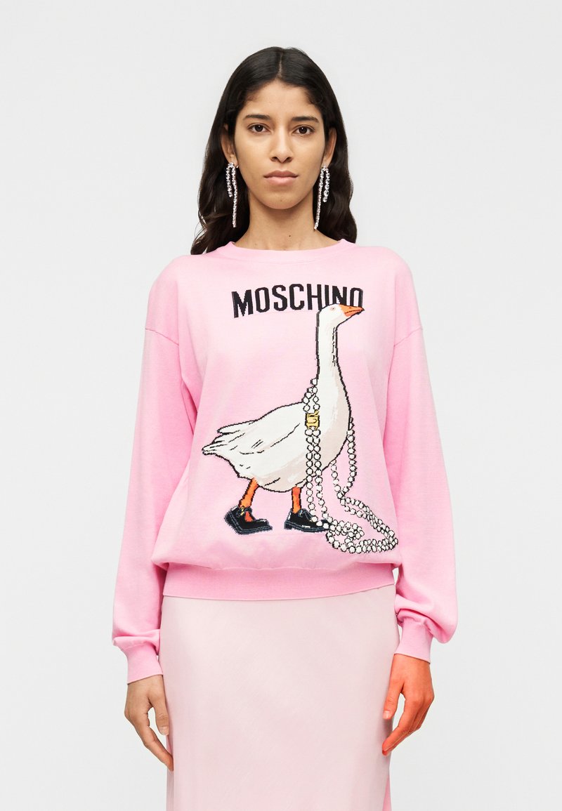 Sweat-shirt en coton rose avec un graphisme d'un canard portant des chaussures noires, orné d'un collier de perles. Texte "Moschino" au-dessus du design.