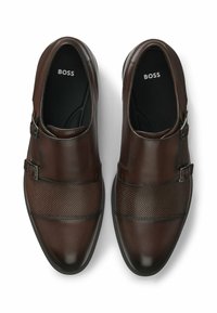 Paar dunkelbraune Lederschuhe mit doppeltem Monk-Strap, strukturierten Zehenkappen und schwarzen Innensohlen mit der Aufschrift "BOSS", von oben betrachtet.
