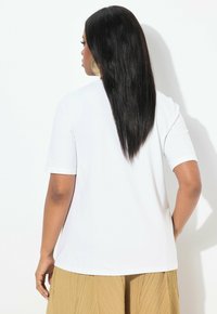 Camiseta blanca de manga corta, con una tela suave, ligera y un corte holgado, combinada con una falda plisada beige.