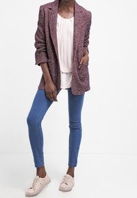 Texturerad rosa och lila blazer, lager-på-lager över en ljusrosa topp, i kombination med blå skinny jeans och beige sneakers. Har två framfickor.